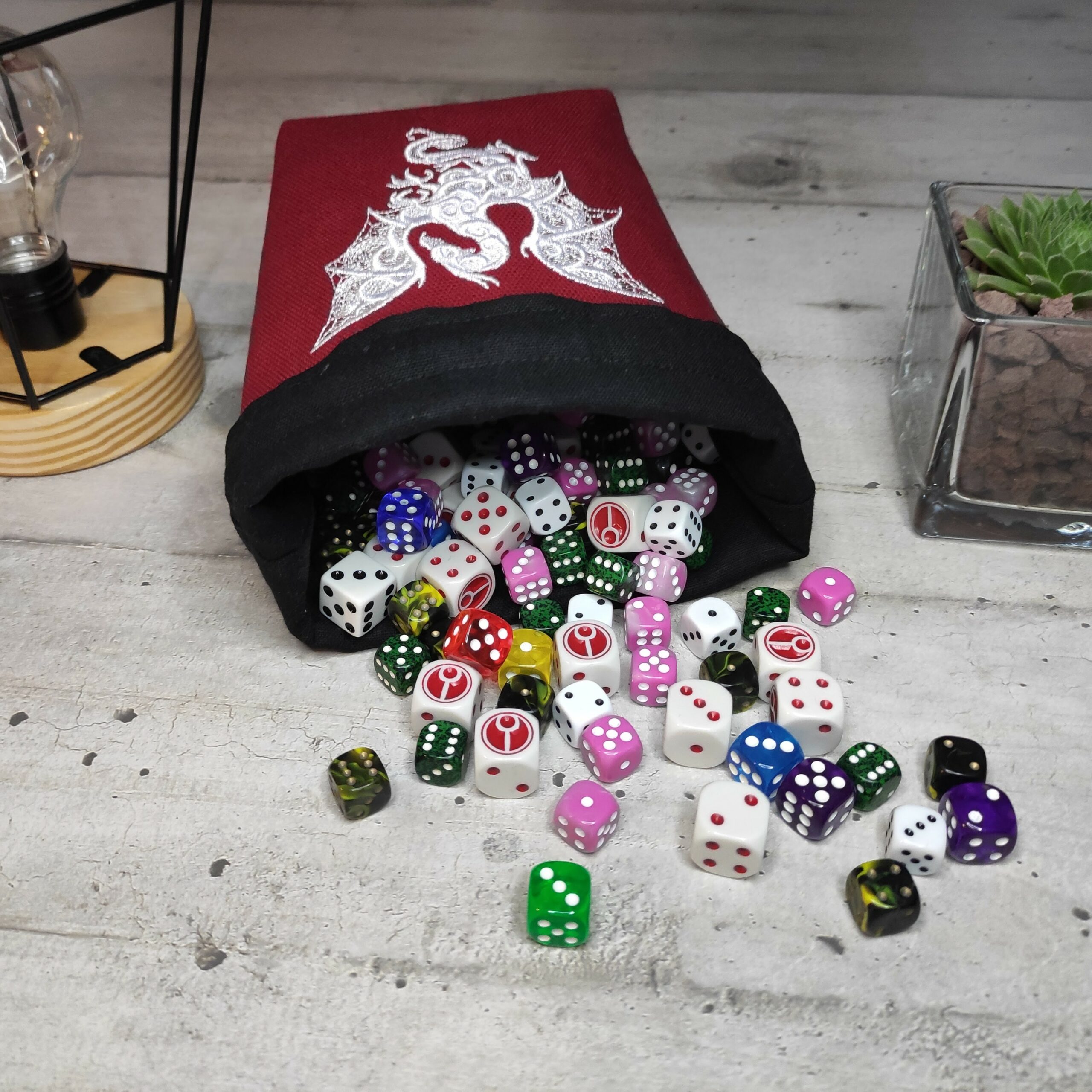 Panière à dés rouge brodée d'un dragon blanc avec intérieur noir contenant plusieurs dizaine de dés
